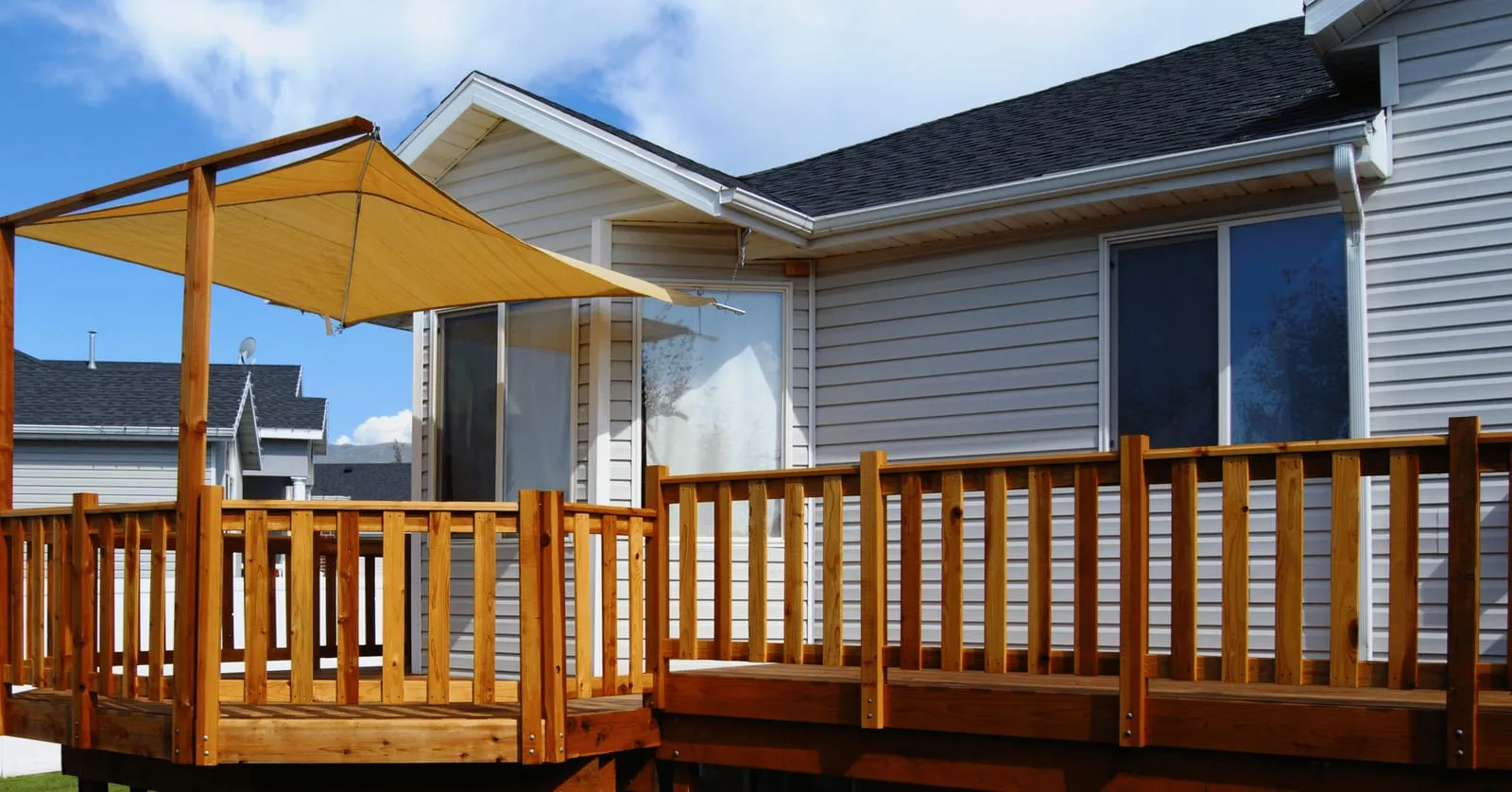 Cedar deck railing with a yellow shade sail beside a grey-sided house