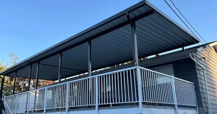 Long metal patio cover over a deck with white aluminum railings beside a house