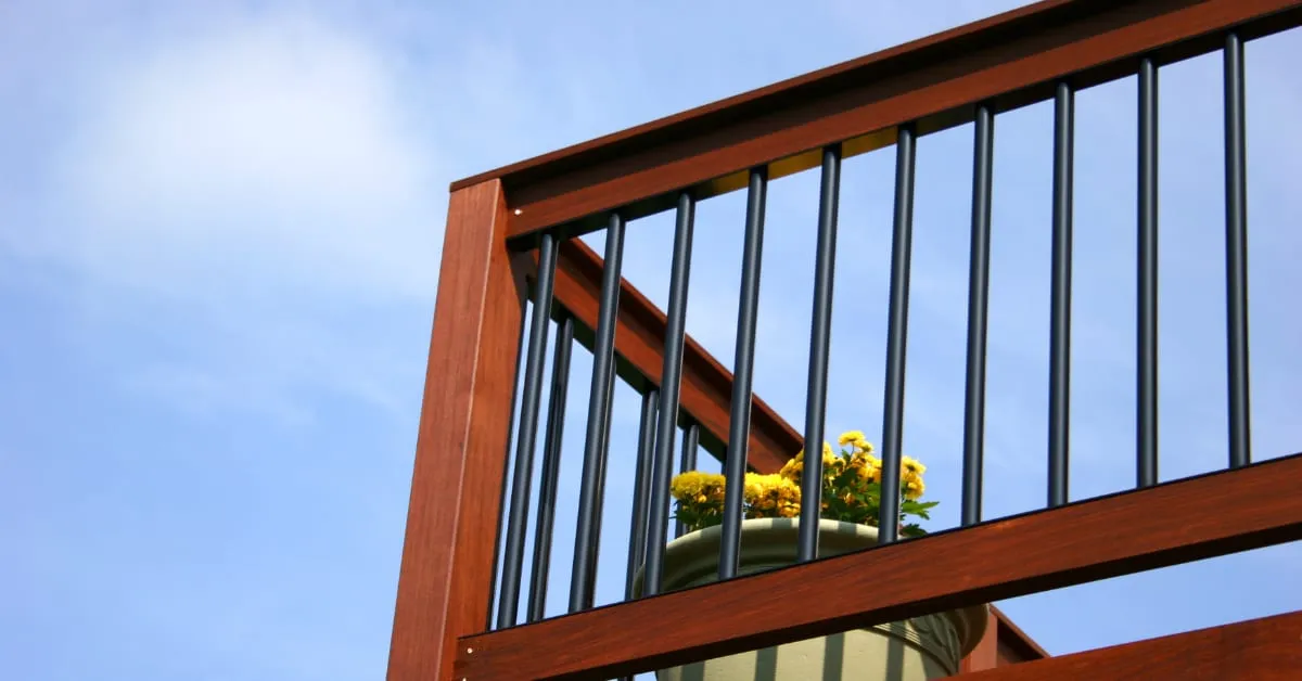 Wood deck railing with black metal balusters against a blue sky