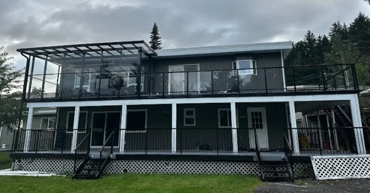 Two-storey house with black railings on both decks and a glass-enclosed corner on top